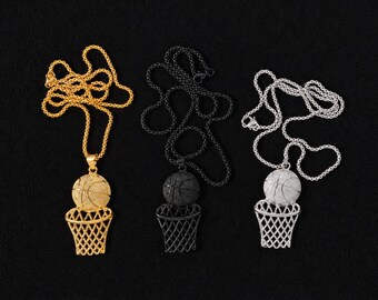 May include: Three basketball pendant necklaces in gold, black, and silver. Each pendant features a detailed basketball above a net, suspended from a matching chain. The pendants are displayed against a black background.