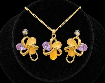 May include: A gold-tone jewelry set consisting of a pendant necklace and matching earrings. Each piece features a flower-shaped design with two yellow oval stones and one purple pear-shaped stone set in a polished gold-colored metal frame.
