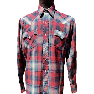 Peut inclure: Une chemise à manches longues boutonnée avec un motif à carreaux rouge, bleu marine et gris. La chemise comprend deux poches de poitrine à rabats pointus, un col classique et des boutons-pression argentés sur la patte avant et les poignets.