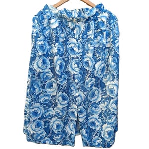 May include: A blue floral button-down shirt with a white rose pattern. The shirt is hanging on a wooden hanger. The floral pattern is a mix of light and dark blue roses.