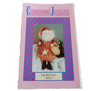 May include: A craft pattern booklet titled Cottonwood Junction featuring a Star Brite Santa 22 inch plump Santa #JW028. The cover shows a fabric Santa doll with a red patterned coat, a matching hat, a white beard, and a hanging star ornament.