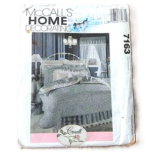 May include: A McCall's Home Decorating sewing pattern envelope, number 7163, featuring a photograph of a bed with a blue and white floral patterned bedspread, ruffled pillows, and a matching bed skirt with lace trim, set in a bedroom.