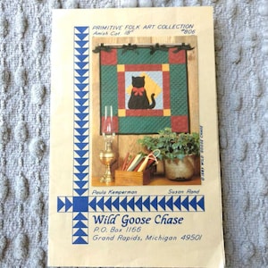 May include: A beige paper pattern envelope titled Primitive Folk Art Collection Amish Cat 18" #806 by Wild Goose Chase. The cover features a photograph of a quilted wall hanging with a black cat, a brass oil lamp, and a wooden box of supplies.