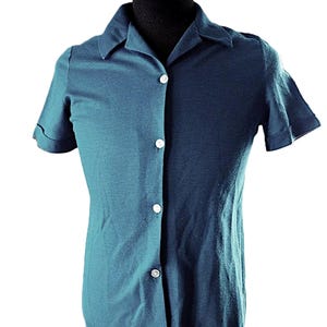 May include: Teal short-sleeved shirt with a collared neckline and three white buttons. The shirt has a classic design and is made of a soft material. The sleeves are cuffed. A versatile addition to any wardrobe.