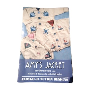 以下が含まれることがあります： 青と赤の航海をテーマにしたデザインが施された、クリーム色のジャケットが3着描かれた本の表紙。テキスト「AMY'S JACKET」は白で表示され、2版でジャケットを装飾するためのデザインが含まれていることを示す追加のテキストがあります。