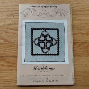 May include: A light pink paper quilt pattern booklet titled Heartstrings by Virginia Robertson from Osage County Quilt Factory. The cover features a central illustration of a square quilt with a dark heart-shaped design and 65" x 65" text.