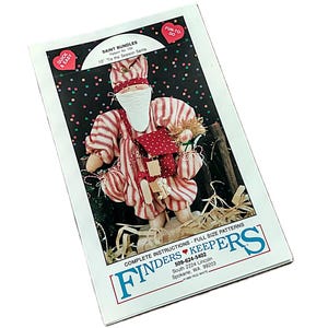 May include: A sewing pattern packet titled Saint Bundles Pattern No. 155 10" 'Tis the Season Santa by Finders Keepers. The cover features a fabric Santa doll in red and white striped clothing with a white beard, holding a small doll, with text.