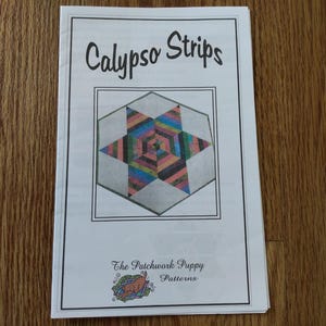 May include: A white paper pattern booklet titled Calypso Strips by The Patchwork Puppy Patterns. The cover features a central graphic of a six-pointed star composed of multicoloured striped fabric segments set within a light grey hexagonal border.
