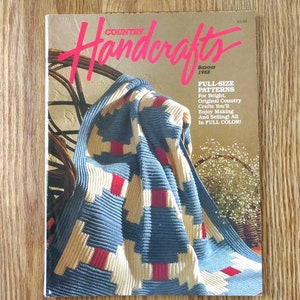 May include: The cover of a vintage magazine, "Country Handcrafts Bazaar 1986", displays a blue, red, and beige quilt over a wicker chair. Text on the cover advertises full-size patterns for crafts.