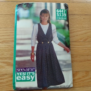 May include: A See & Sew sewing pattern envelope 6447 for a sleeveless, V-neck, polka-dot jumper dress with two gold-tone buttons at the waist. The pattern is labelled size C (18-20-22) and features the text Yes! It's Easy on the front cover.