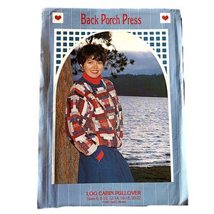 May include: A vintage magazine cover featuring a woman wearing a patchwork sweater. The cover has the text "Back Porch Press" and "LOG CABIN PULLOVER" with size details. The background shows a lake and trees.
