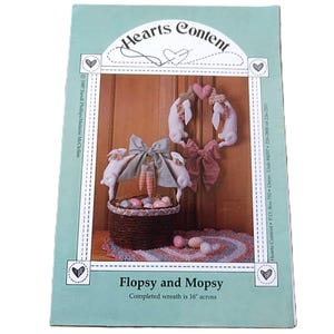 May include: A craft pattern booklet titled Hearts Content featuring Flopsy and Mopsy. The cover displays a brown woven basket filled with pastel eggs, a fabric bow, and two white rabbit figures, alongside a wreath with a pink heart and rabbits.