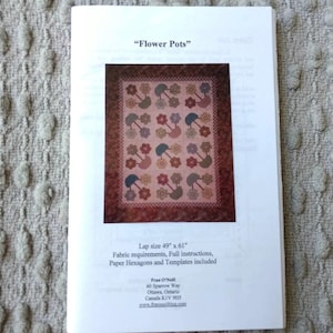 May include: A white instructional booklet titled Flower Pots featuring a quilt pattern with a pink background, floral motifs, and a dark brown border. The text indicates a lap size of 49 inches by 61 inches, including fabric requirements and templates.