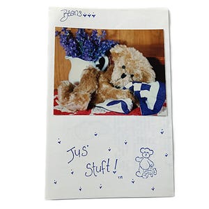May include: A white rectangular card featuring the word Beans at the top and the text Jus Stuft! with a small line drawing of a teddy bear below. A photograph shows a tan teddy bear resting next to a white pitcher of purple flowers.