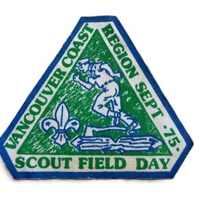 Peut inclure: Un écusson triangulaire avec une bordure bleue et un dos blanc. L'écusson présente un texte vert qui dit "Vancouver Coast Region Sept '75" et "Scout Field Day". Une illustration blanche et bleue d'un scout en course est au centre.