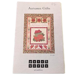 May include: A printed paper with the title "Autumn Gifts" and a quilt design. The quilt features a basket of apples, fall leaves, and carrots. The words "Autumn Gifts" are repeated in the design. The bottom of the paper has the words "patch works studio".