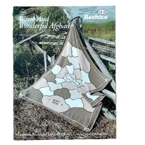 May include: A vintage book cover titled "Warm And Wonderful Afghans" featuring a geometric patterned afghan in shades of brown, beige, and white. The afghan is draped over a wooden fence, with the book's title and a price tag visible.