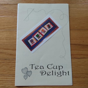 Peut inclure: Une carte crème avec le texte "Tea Cup Delight" et trois cœurs gris. Une image rectangulaire de quatre tasses à thé est centrée sur la carte, avec un motif d'aiguille et de fil au-dessus. Les tasses à thé sont rouges, vertes et bleues.