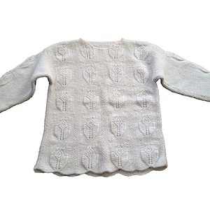 May include: An off-white long-sleeve knit sweater featuring a repeating embossed tulip pattern across the front and sleeves. The garment has a round neckline, long sleeves with cable knit detailing, and a scalloped hemline finish.