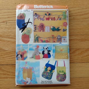 May include: A Butterick sewing pattern featuring various stuffed animal designs, including a bear in a stocking, a panda, a seal, and a frog. The pattern also includes designs for a toy organizer, a pillow, and tote bags. The text "Toys not included" is visible.