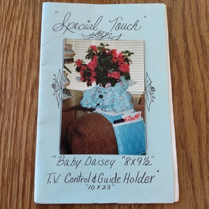 May include: A light blue brochure with the text "Special Touch" and "Baby Daisey 8x9 1/2". The brochure features a photo of a blue dog-shaped TV control holder, measuring 10 x 23 inches, with a plant on top.