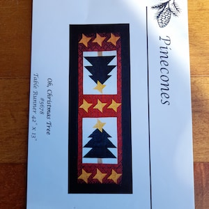 以下が含まれることがあります： 黒いクリスマスツリーと金色の星が白い背景に繰り返されるデザインの、クリスマスをテーマにしたテーブルランナーのパターン、107 x 33 cm。赤と黒のボーダーで縁取られています。テキストは「Oh, Christmas Tree」と書かれています。