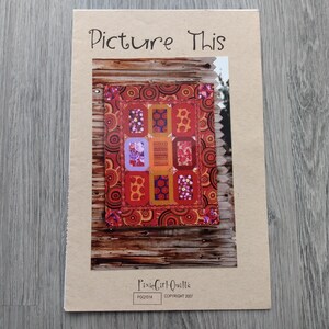 May include: A rectangular instructional booklet titled Picture This by PixieGirl Quilts. The cover features a photograph of a quilt with red, orange, and purple rectangular blocks surrounded by a border with circular patterns against a wooden background.