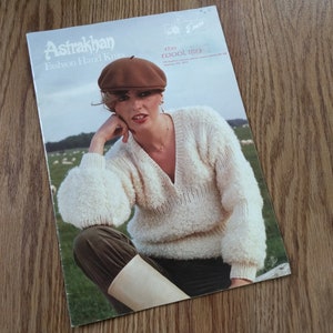 May include: A vintage Astrakhan Fashion Hand Knits pattern booklet featuring a person wearing a brown beret and a white textured V-neck sweater with long sleeves. The cover includes the text Astrakhan Fashion Hand Knits and The Wool Man.