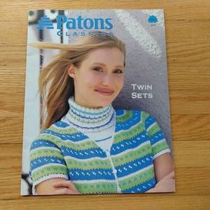 May include: A magazine cover featuring a woman wearing a blue, green, and white patterned sweater and turtleneck. The magazine is titled "Patons Classics" with the words "Twin Sets" displayed.