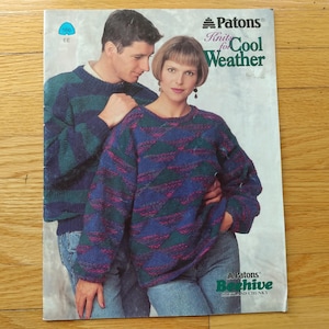 May include: A vintage Patons knitting pattern booklet titled Knits for Cool Weather, featuring a photograph of two people wearing long-sleeved sweaters with a geometric pattern in shades of blue, green, and magenta, paired with blue denim jeans.