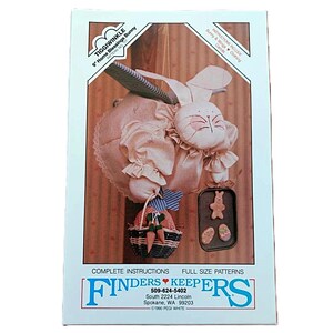 May include: A craft pattern package titled Tiggiwinkle 9" Home Blessings Bunny by Finders Keepers. The cover features a beige fabric bunny with wings, holding a small basket with carrots and a tray of cookies. Includes instructions and full-size patterns.