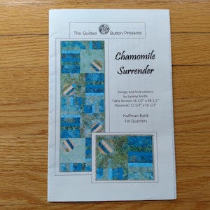May include: A printed pattern for a table runner and placemat, titled "Chamomile Surrender." The design features a blue and green patchwork pattern. The table runner measures 42 x 123 cm, and the placemat is 32 x 42 cm.