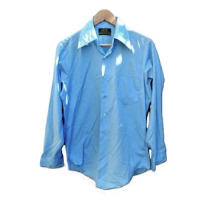 May include: Light blue long-sleeve shirt with a pointed collar and a chest pocket. The shirt is buttoned down the front and is hanging on a wooden hanger. The shirt is made of a lightweight fabric.