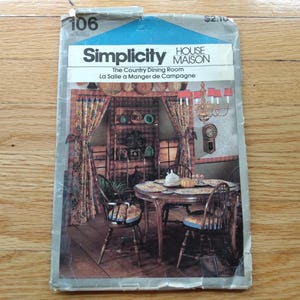 May include: A Simplicity House Maison sewing pattern envelope, number 106, titled The Country Dining Room. The cover features a photograph of a dining room with a wooden table, chairs, floral curtains, a chandelier, and a wall clock.
