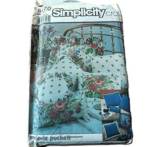 May include: A Simplicity craft sewing pattern envelope featuring illustrations of various decorative pillows. The front shows floral print pillows with ruffles and solid blue pillows. The text includes Simplicity craft and Marjorie Puckett.
