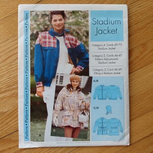May include: A sewing pattern for a stadium jacket. The pattern features a blue jacket with plaid accents, and a second jacket in a camouflage pattern. The text "Stadium Jacket" is displayed in a blue box.