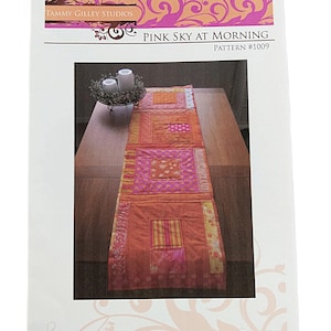 May include: A sewing pattern instruction sheet titled Pink Sky at Morning Pattern #1009 by Tammy Gilley Studios. The cover features a photograph of a rectangular quilted table runner in shades of orange, pink, and yellow with square blocks.