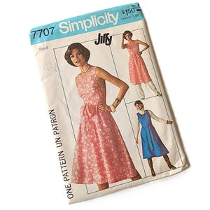 May include: A Simplicity 7707 Jiffy sewing pattern envelope for a sleeveless dress. The cover features illustrations of a pink floral dress with a waist tie, a pink floral dress over white trousers, and a blue dress over a white turtleneck sweater.