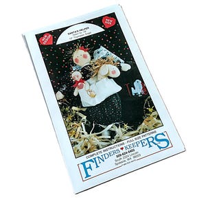 May include: A sewing pattern envelope titled Santa's Helper 10" Toymaker Angel by Finders Keepers. The cover features a photograph of a handmade fabric doll with a black dress, red cheeks, and straw hair, holding a smaller doll against a dark background.