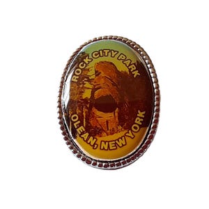 May include: Oval souvenir pin depicting Rock City Park in Olean, New York. The pin has a silver beaded edge and the text "Rock City Park, Olean, New York".