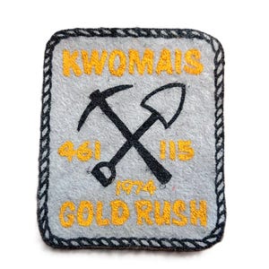 May include: A square, grey patch with a black border and the text "KWOMAIS" in yellow. A crossed pickaxe and shovel are in the centre. Below are the numbers "461" and "115", and the text "1974 GOLD RUSH".