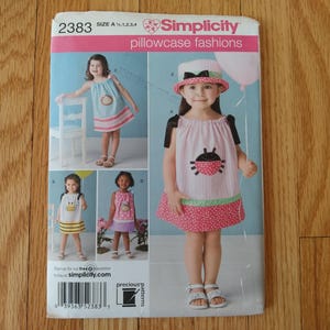 May include: Simplicity pillowcase fashions sewing pattern. The pattern features images of children's dresses with various designs, including a ladybug and striped patterns. The pattern number is 2383, and the sizes are A 1,2,3,4.