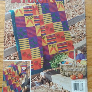 May include: A Patons knitting pattern book cover featuring a colorful blanket design with squares of carrots and tomatoes. The blanket is draped over a wooden fence. A basket of vegetables and tomatoes is also shown.