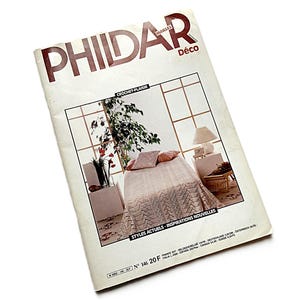May include: A vintage "PHILDAR Déco" magazine featuring crochet patterns. The cover displays a bedroom scene with a crocheted bedspread, pillows, and a lamp. The magazine is slightly angled on a white background.