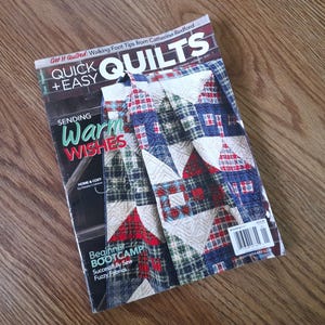 May include: A magazine titled Quick + Easy Quilts featuring a cover image of a patchwork quilt with red, blue, and white plaid and solid fabric squares. The cover text includes Sending Warm Wishes, Beginner Bootcamp, and Successfully Sew Fuzzy Fabrics.