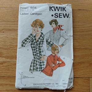 May include: A vintage Kwik Sew pattern for a ladies' cardigan. The pattern envelope features illustrations of three different cardigan styles. The main illustration shows a woman in a black and white houndstooth cardigan. The text on the envelope reads "Ladies' Cardigan."
