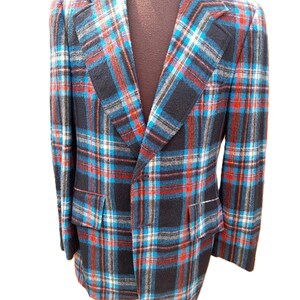 May include: A blazer featuring a plaid pattern in black, bright blue, and red. The garment has notched lapels, long sleeves, and two front flap pockets. The fabric has a textured appearance, and the jacket is displayed on a brown mannequin torso.