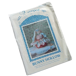 May include: A white paper sewing pattern envelope titled all. cooped. up. BUNNY HOLLOW with blue text and a blue decorative border. The centre features a photograph of a fabric bunny doll wearing a floral dress, with the number 500 printed in the corner.