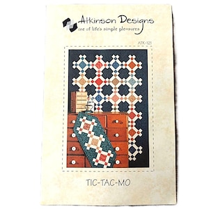 May include: A printed pattern for a quilt project titled "TIC-TAC-MO" by Atkinson Designs. The cover shows a quilt design with a dark blue background and colourful diamond shapes. The pattern includes a table runner design.