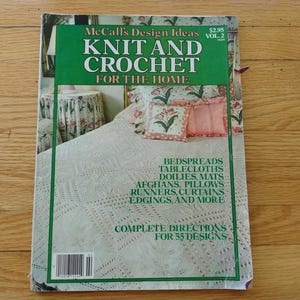 May include: A McCall's Design Ideas Knit and Crochet for the Home Vol. 2 magazine featuring a white crocheted bedspread, floral pillows, and a table with a floral cloth. The cover text lists bedspreads, tablecloths, doilies, mats, afghans, pillows, runners, curtains, edgings, and more.